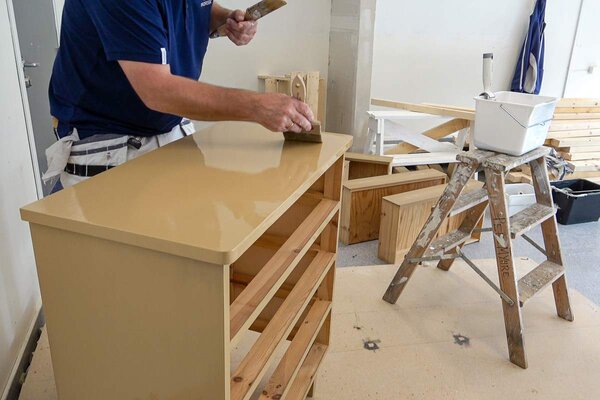 Per pusser og maler en kommode i verkstedet